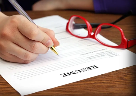 woman writing on paper with glasses on table